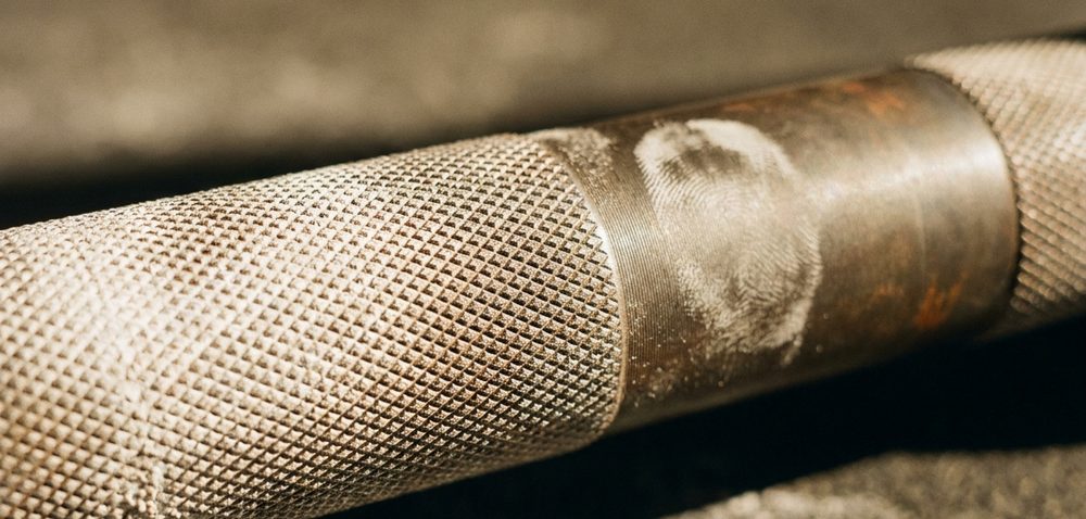 Close view of chalk packed into the knurling of a steel barbell, with a chalk thumbprint on the shaft